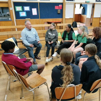 Students from Whitestone Kāhui Ako schools are gathered around an Inspiring the Future role model who is talking to them about his job